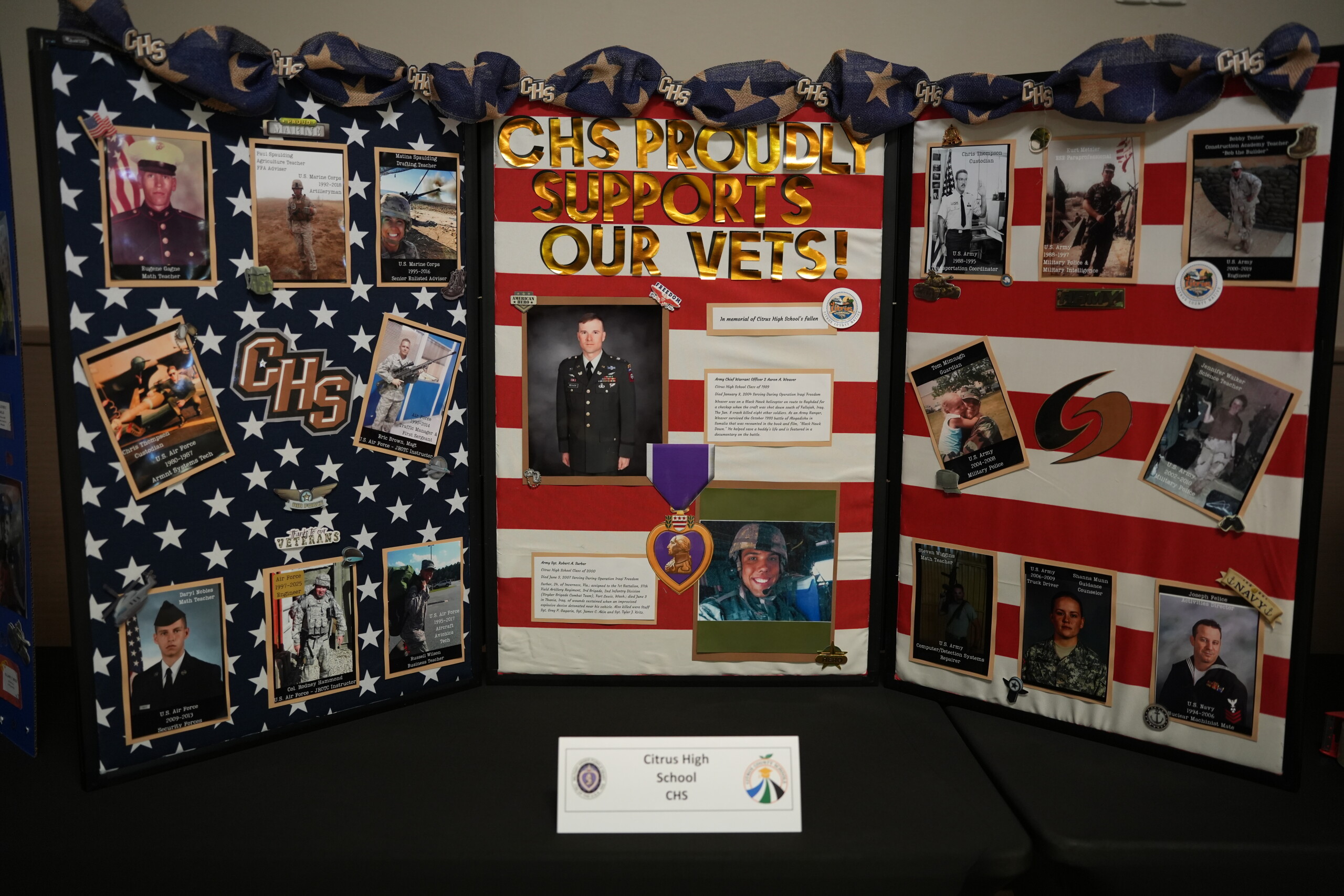 A trifold display board decorated with an American flag theme reads, "CHS PROUDLY SUPPORTS OUR VETS!" and features photos of service members.